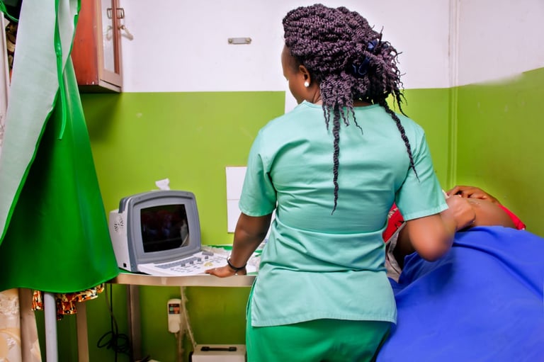 Healthcare worker in turquoise scrubs operating an ultrasound machine in a medical examination room with green walls