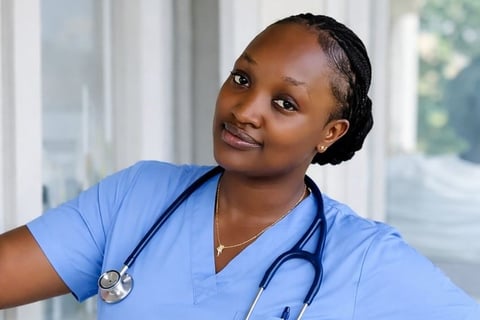 Healthcare professional wearing blue scrubs and stethoscope smiling at camera in clinical setting
