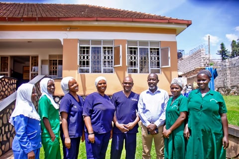 Group of healthcare workers in scrubs standing in front of a yellow clinic building with a stone foundation