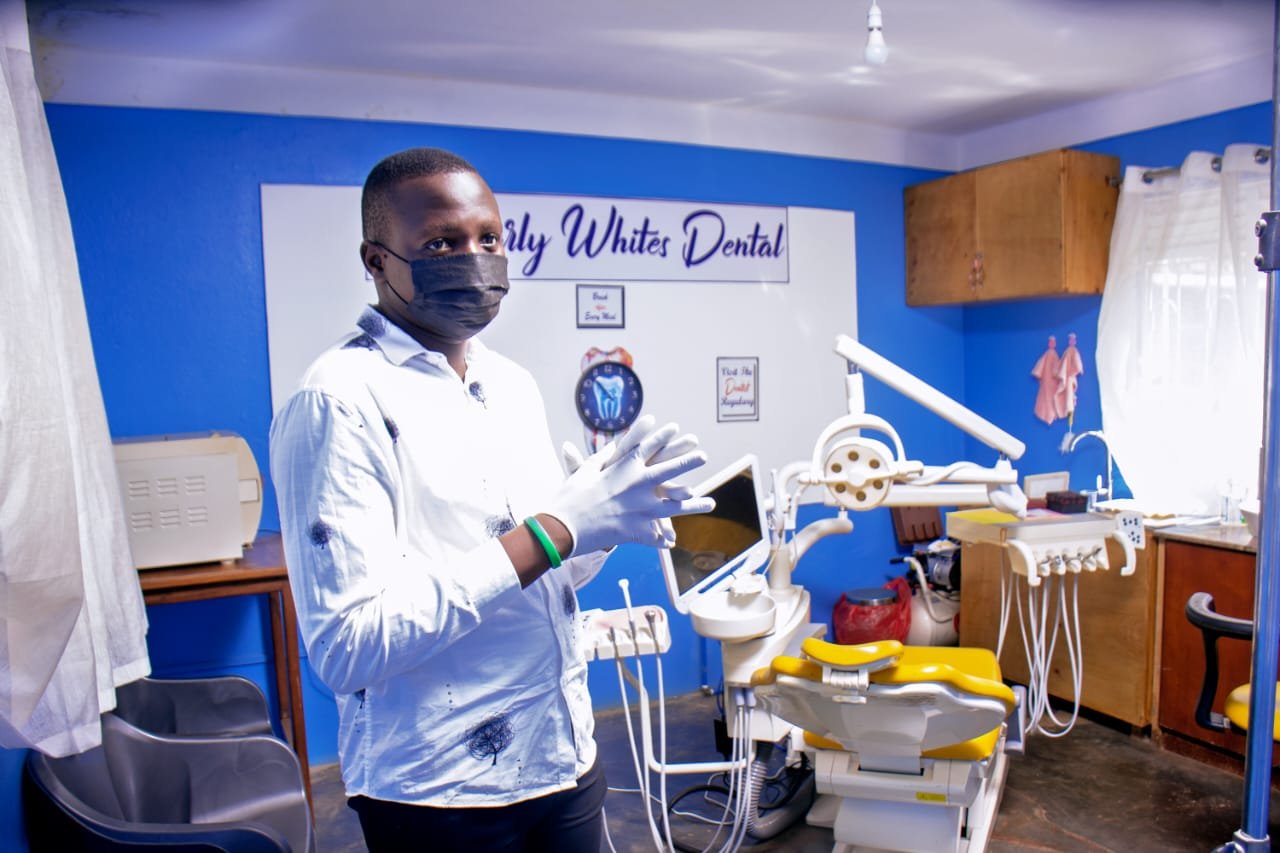 Dentist in mask and gloves holding dental model in operatory with blue walls and dental equipment
