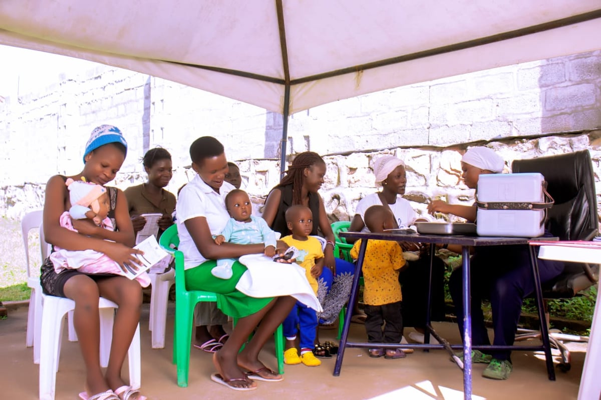 Group of children sitting under a pink tent eating food, with shelves and supplies visible in the background