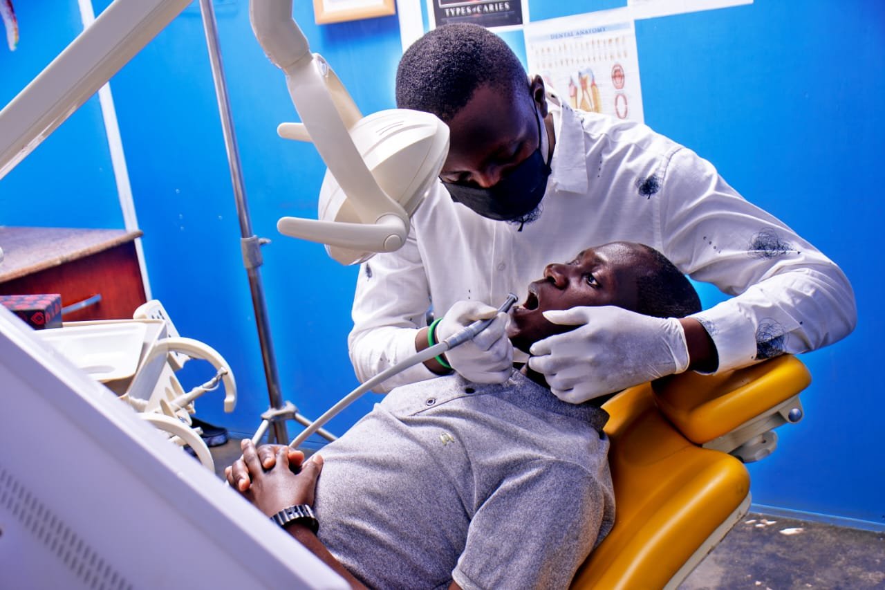Dentist in white coat and mask examining a child patient in dental chair with yellow headrest against blue background