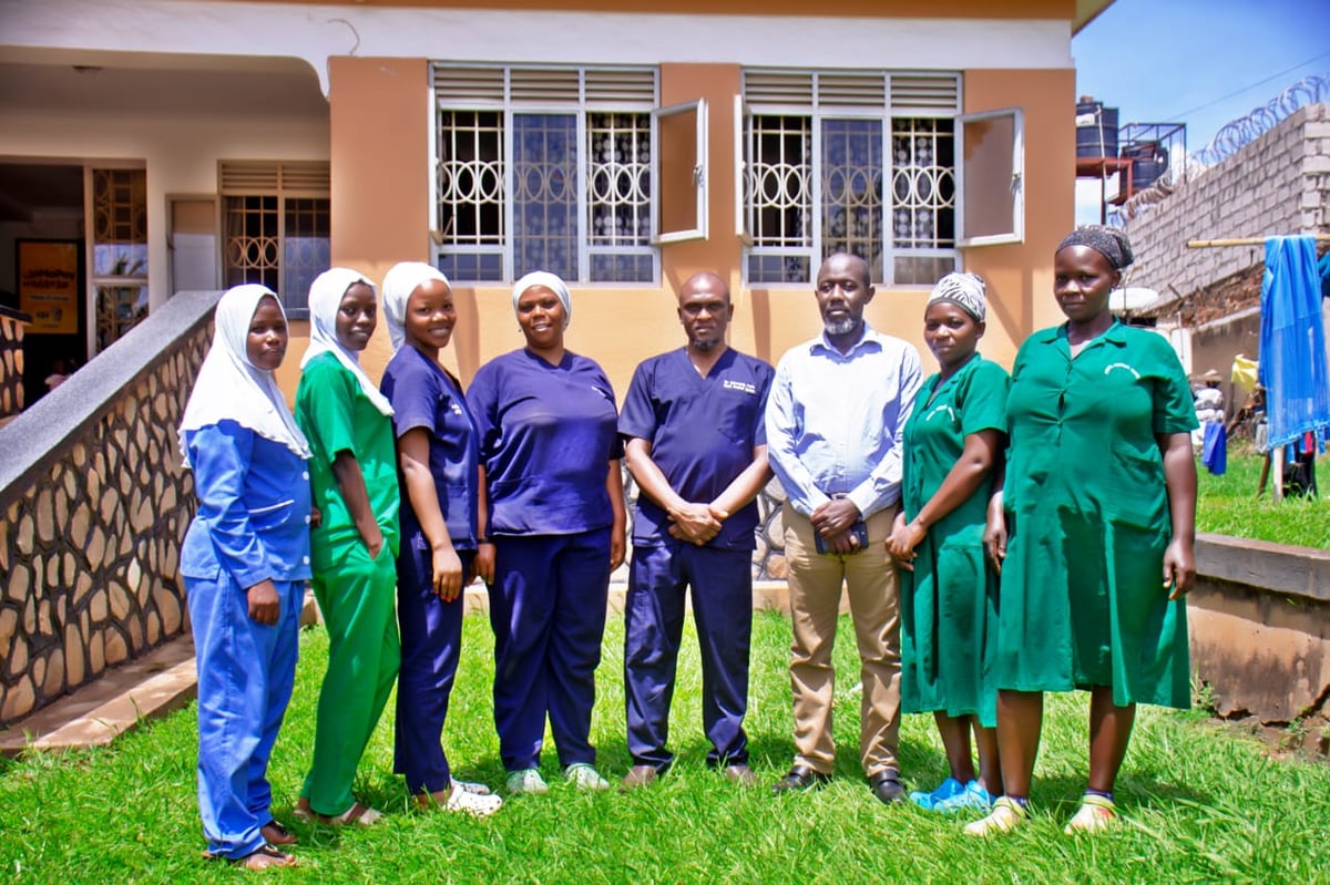 Group of healthcare workers in colorful uniforms standing together on grass in front of a yellow building