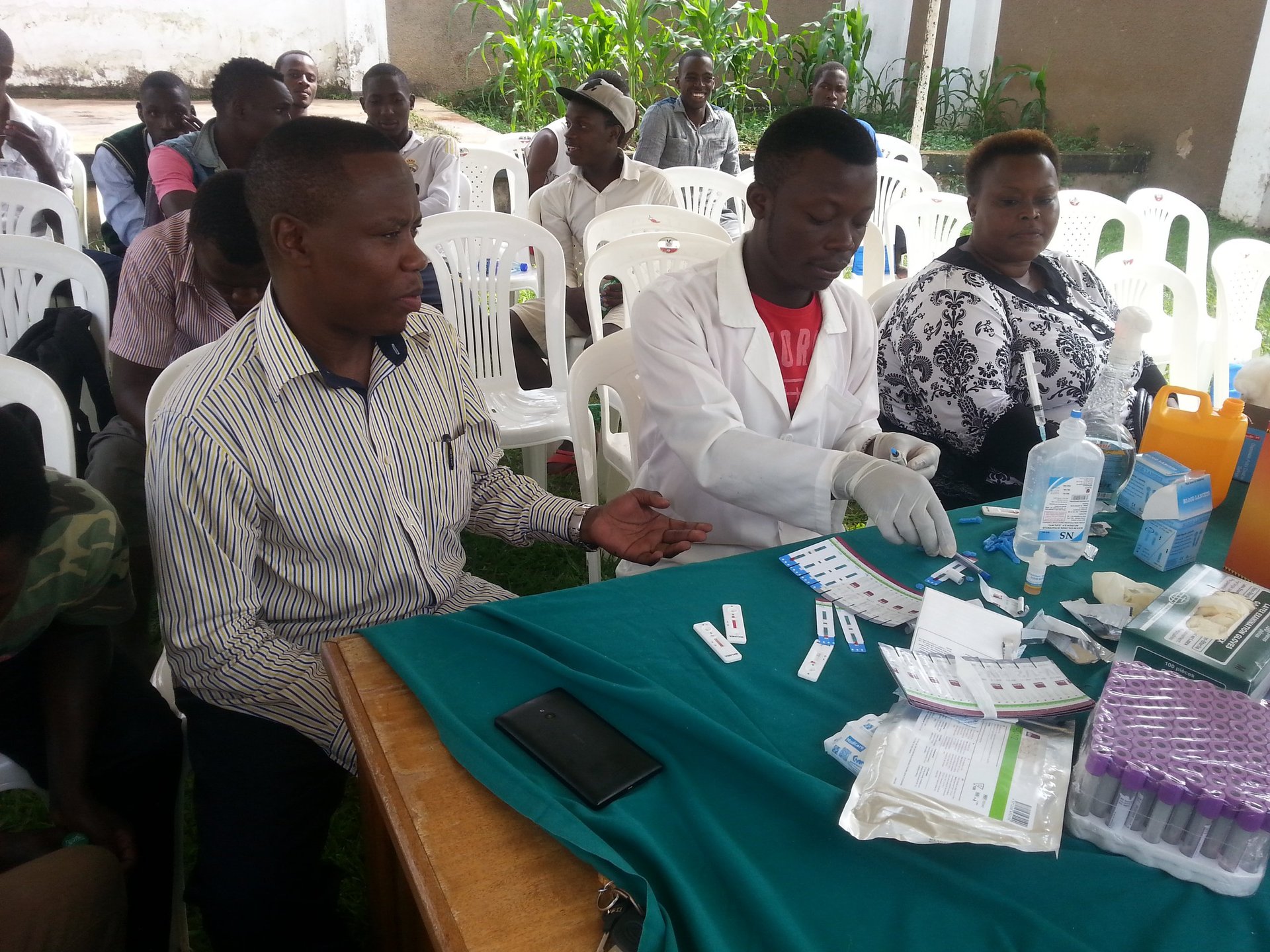 Men seated at a table during an outdoor health or community event with medical supplies