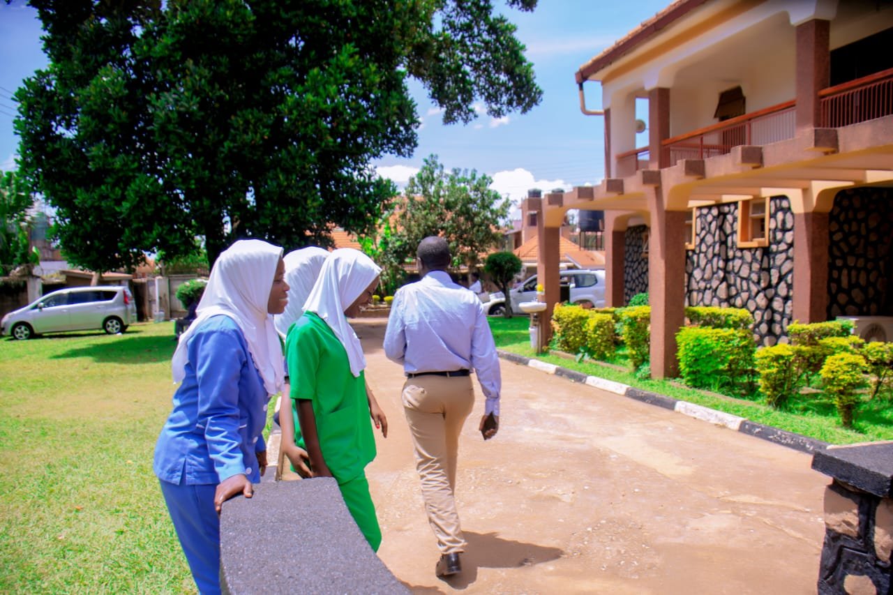 Three people walking toward a residential building on a tree-lined pathway with green lawn and manicured bushes