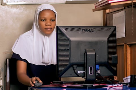 Young woman wearing white headscarf and black shirt sitting at desk with desktop computer monitor