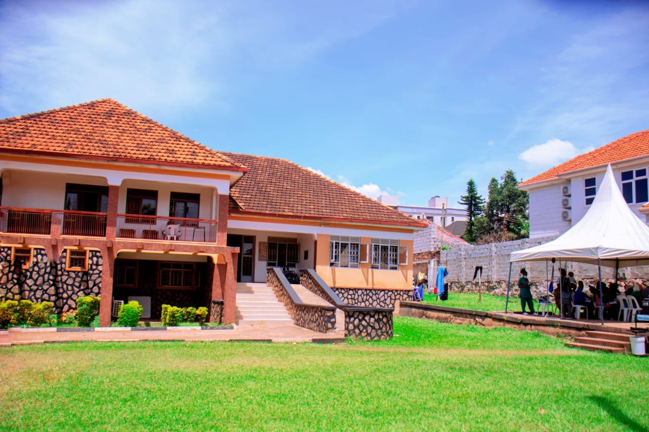 Modern residential compound with terracotta-roofed buildings, manicured lawn, and white event tent under blue sky